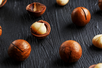 Obraz premium Purified and shell repeats macadamia nuts on black textural stone background. Healthy eating concept