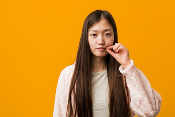 Young chinese woman in pajama with fingers on lips keeping a secret.
