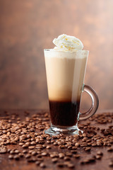 Glass cup with coffee and coffee beans on a brown background.