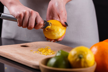 young woman in a gray aprons cuts lemon zest