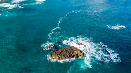 Waves breaking on a small rock on sunny day. Auckland, New Zealand