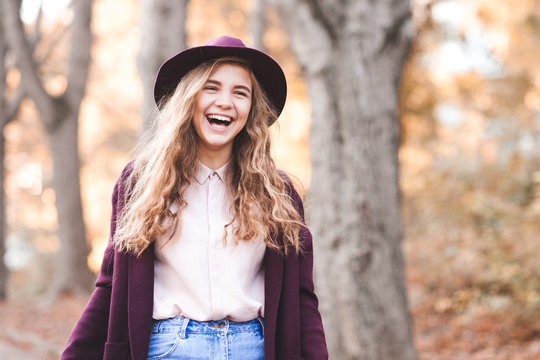 Laughing teen girl 14-16 year old wearing hat and jacket walking in park. Looking at camera. Teenagerhood.