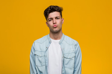 Obraz premium Young handsome student wearing a denim shirt blows cheeks, has tired expression. Facial expression concept.