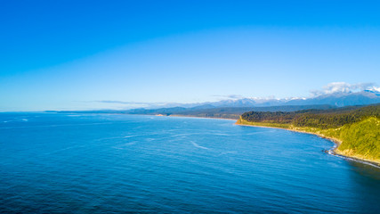 Fototapeta na wymiar Ocean bay on a sunny day with green peninsula on the background. West Coast, South Island, New Zealand
