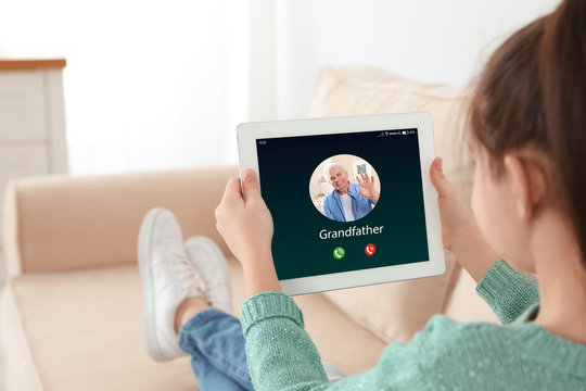 Closeup view of little girl using tablet for conversation with grandfather via video chat at home