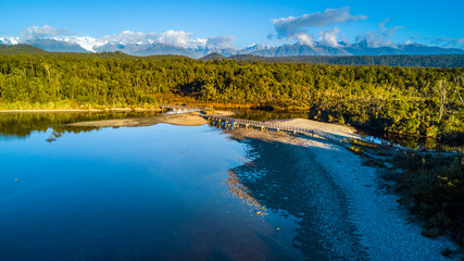 Small bridge across a river surrounded by native forest at the coastline of Tasman sea. West Coast, South Island, New Zealand