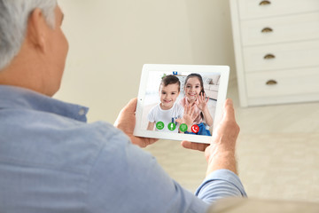 Closeup view of senior man talking with grandchildren via video chat at home