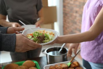 Poor man receiving food from volunteer indoors, closeup