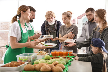 Volunteers giving food to poor people indoors