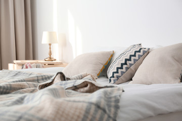 Bed with pillows and plaid near light wall. Cozy interior design