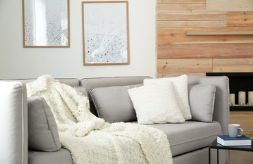 Cozy sofa with pillows and plaid near decorative fireplace in living room. Interior design