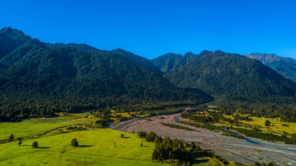 Fototapeta na wymiar River running through sunny valley with high mountains on the background. West Coast, South Island, New Zealand