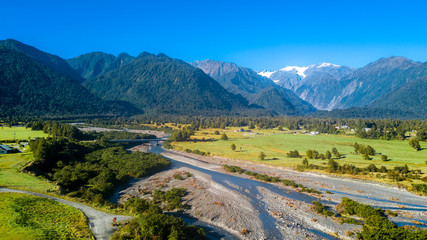 River running through sunny valley with high mountains on the background. West Coast, South Island, New Zealand