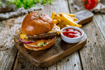 Hamurger with fries and ketchup on board and wooden background