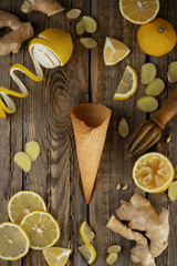 ginger lemon ice cream in a waffle cone with fresh lemons and ginger slices on a dark wooden background of boards 