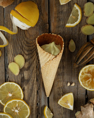 ginger lemon ice cream in a waffle cone with fresh lemons and ginger slices on a dark wooden background of boards 