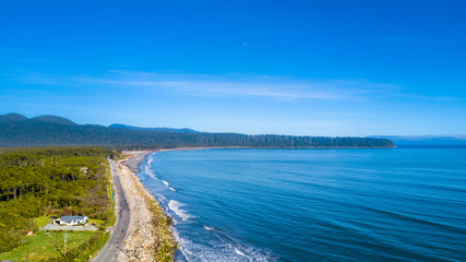 Road running along a sunny beach with a peninsula and mountains on the background. West Coast, South Island, New Zealand