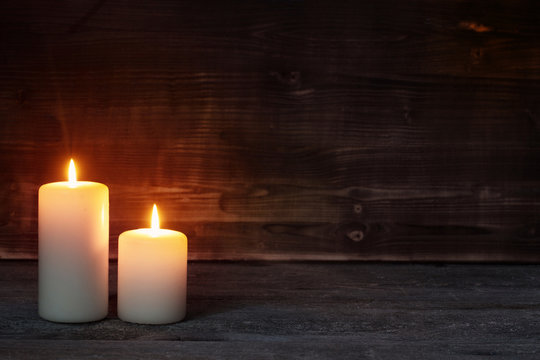 Burning candle on old wooden background
