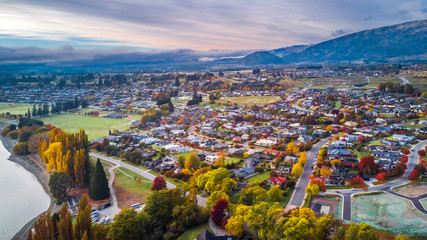 Small town surrounded by yellow autumn trees at the foot of mountain ridge. Wanaka, Otago, South...