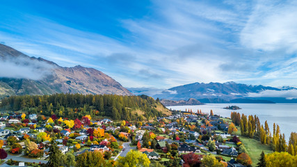 Small town surrounded by yellow autumn trees on a shore of pristine lake with mountains on the...