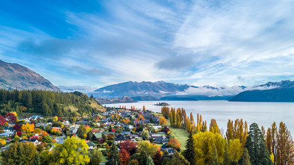 Small town surrounded by yellow autumn trees on a shore of pristine lake with mountains on the...