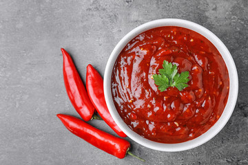 Bowl of hot chili sauce with parsley and red peppers on grey background, flat lay. Space for text