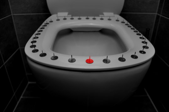 Silver big thumbtacks or drawing-pins and one red tack on toilet bowl seat.Hemorrhoids or urine problem concept. White toilet seat with tacks.