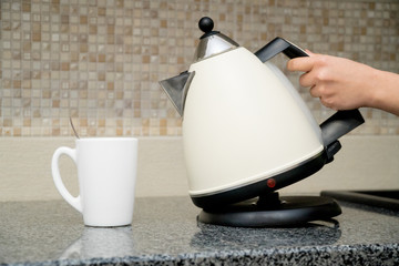 The woman's hand holds electric glass kettle on a domestic kitchen