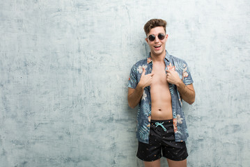 Fototapeta na wymiar Young caucasian man wearing a swimsuit surprised pointing at himself, smiling broadly.