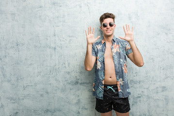 Fototapeta na wymiar Young caucasian man wearing a swimsuit showing number ten with hands.