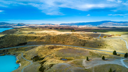 Road running through hills and forest with mountain range on the background. Otago, South Island, New Zealand