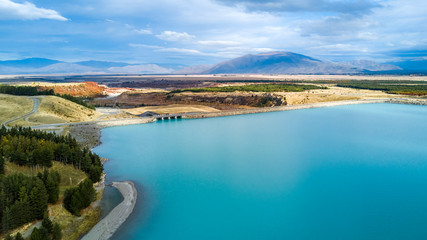 Obraz premium Road running across a bridge through hills and forest with mountain range on the background. Otago, South Island, New Zealand