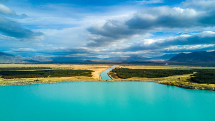 Beautiful lake and a water channel running through hills and forest with mountain range on the background. Otago, South Island, New Zealand