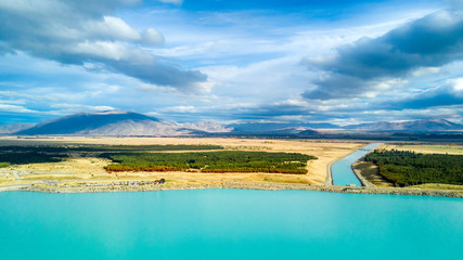Beautiful lake and a water channel running through hills and forest with mountain range on the background. Otago, South Island, New Zealand