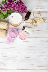 Fototapeta na wymiar Spa and bath cosmetics with lilac flowers. Bath salt, soap, cream, oil, serum and towel rolls on wooden rustic background. Organic natural cosmetics. Fresh care of body. Baner with copy space top view