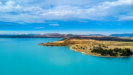 Fototapeta na wymiar Hills on a shore of a beautiful lake with mountain range on the background. Otago, South Island, New Zealand