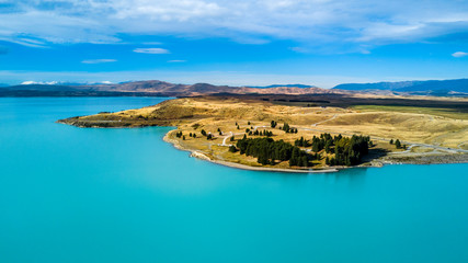 Fototapeta premium Hills on a shore of a beautiful lake with mountain range on the background. Otago, South Island, New Zealand