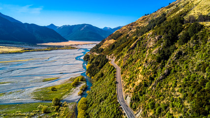 Road running on the rocky cliff along a river with mountains on the background. West Coast, South Island, New Zealand © Dmitri