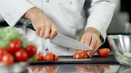 Chef male cutting tomato at restaurant kitchen. Closeup chef cooking fresh food.