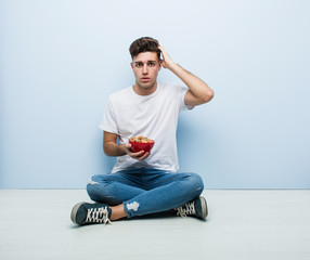 Young man eating cereals sitting on the floor being shocked, she has remembered important meeting.