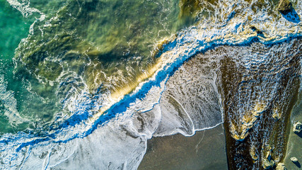 River braking through the surf on a remote ocean beach. West Coast, South Island, New Zealand