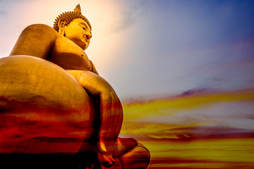 The large golden lord of Buddha statue that is faithful on a beautiful and colourful sky with orange, yellow, red, blue.