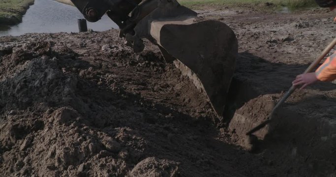 close up digger digging trench and man whith spade helps