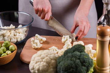 young woman in a gray aprons cuts cauliflower broccoli