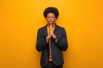 Young business african american man over an orange wall praying very happy and confident