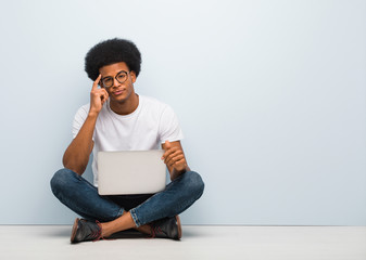 Young black man sitting on the floor with a laptop thinking about an idea