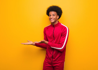 Young sport black man over an orange wall holding something with hands