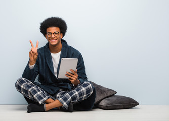 Young black man sitting on his house and holding his tablet fun and happy doing a gesture of victory