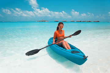 Sexy brunette paddling a kayak. Woman exploring calm tropical bay. Maldives. Sport, recreation. Summer water sport, adventure outdoors.