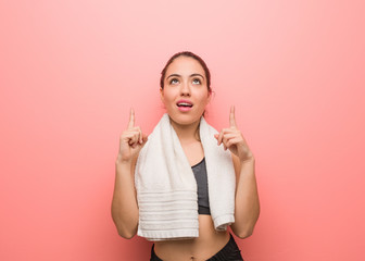 Young fitness woman surprised pointing up to show something